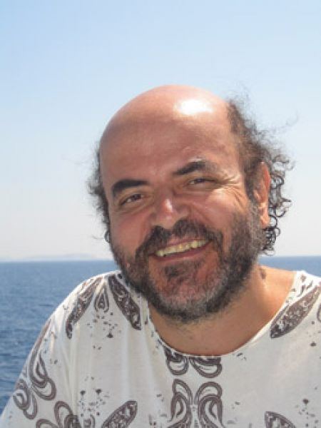 Uśmiechnięty Christos Papadimitriou na tle morza w białej letniej koszuli.