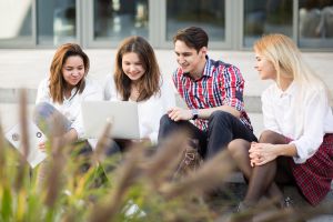 Studenci siedzący przed wydziałem na schodach z laptopem