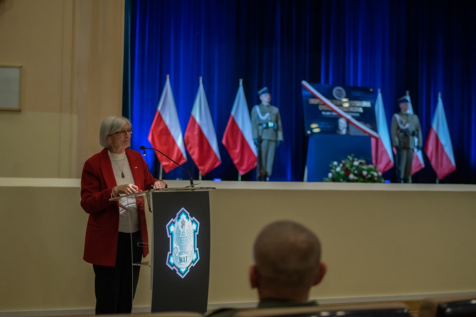 profesor Magdalena Jaroszewska głosząca mowę podczas uroczystości, w tle tablica oraz żołnierze.