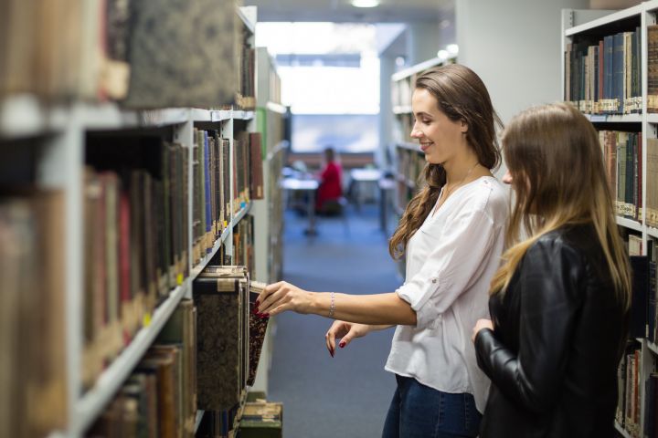 Studentki wyciągają książkę z półki w bibliotece