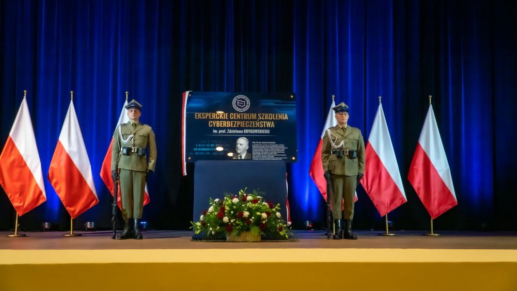 Zdjęcie z uroczystości nadania imienia Eksperckiemu Centrum Szkolenia Cyberbezpieczeństwa. Na zdjęciu dwoje żołnierzy stojących przy tablicy ze zdjęciem prof. Krygowskiego