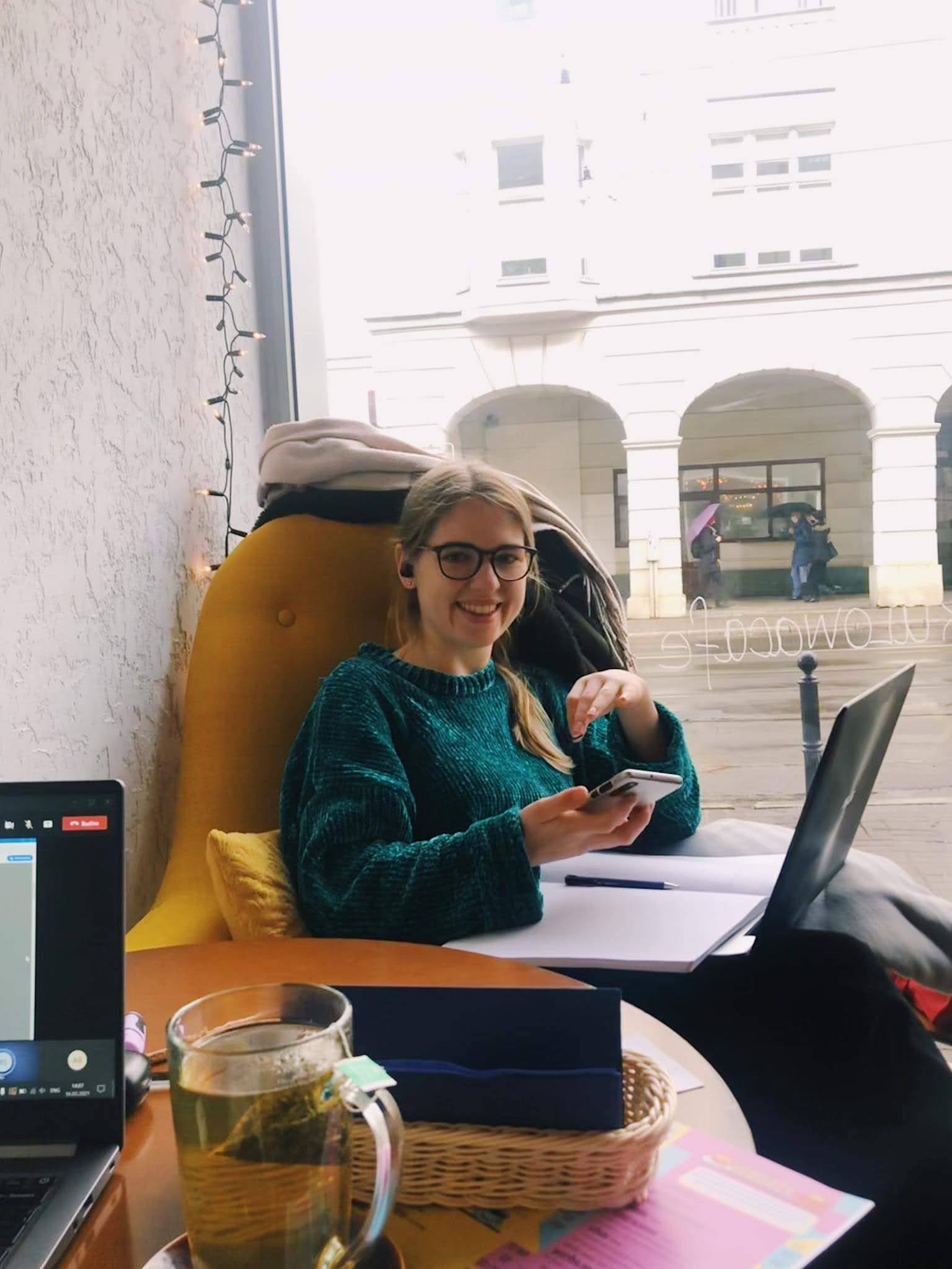 Dziewczyna siedząca w kawiarni przed laptopem, z telefonem w ręce